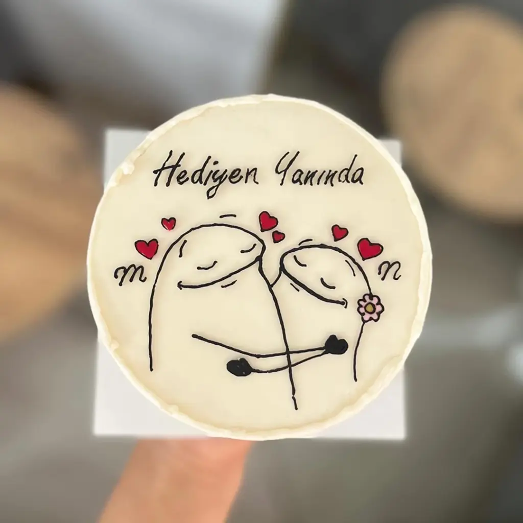 Hediye Yanında yazılı, sarılan Flork karakterleri, kırmızı kalpler ve çiçek detaylı krem renkli yuvarlak pasta.