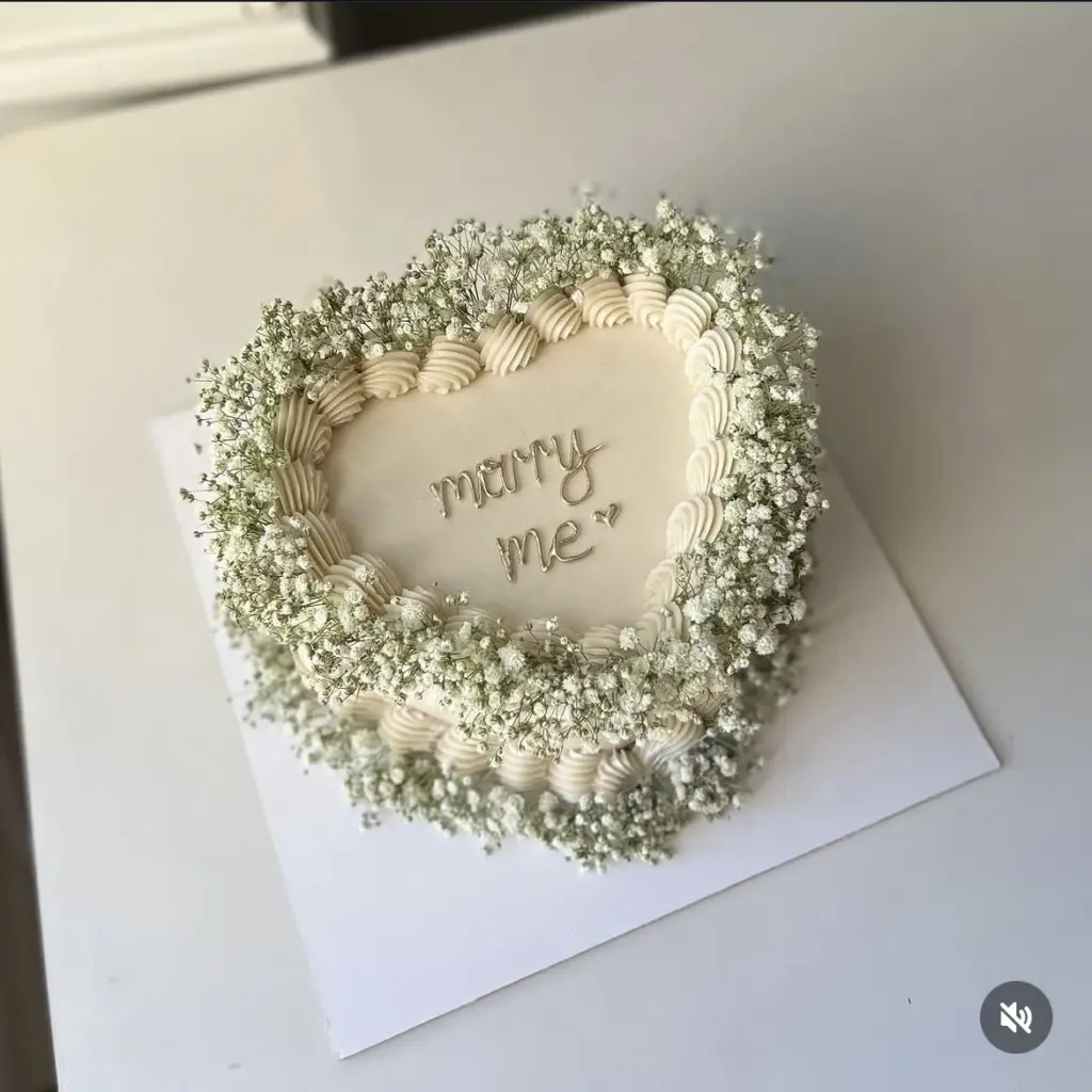 Krem rengi, kalpli, gipsofilya çiçekleri ve marry me yazısıyla süslenmiş özel tasarım nişan pastası.