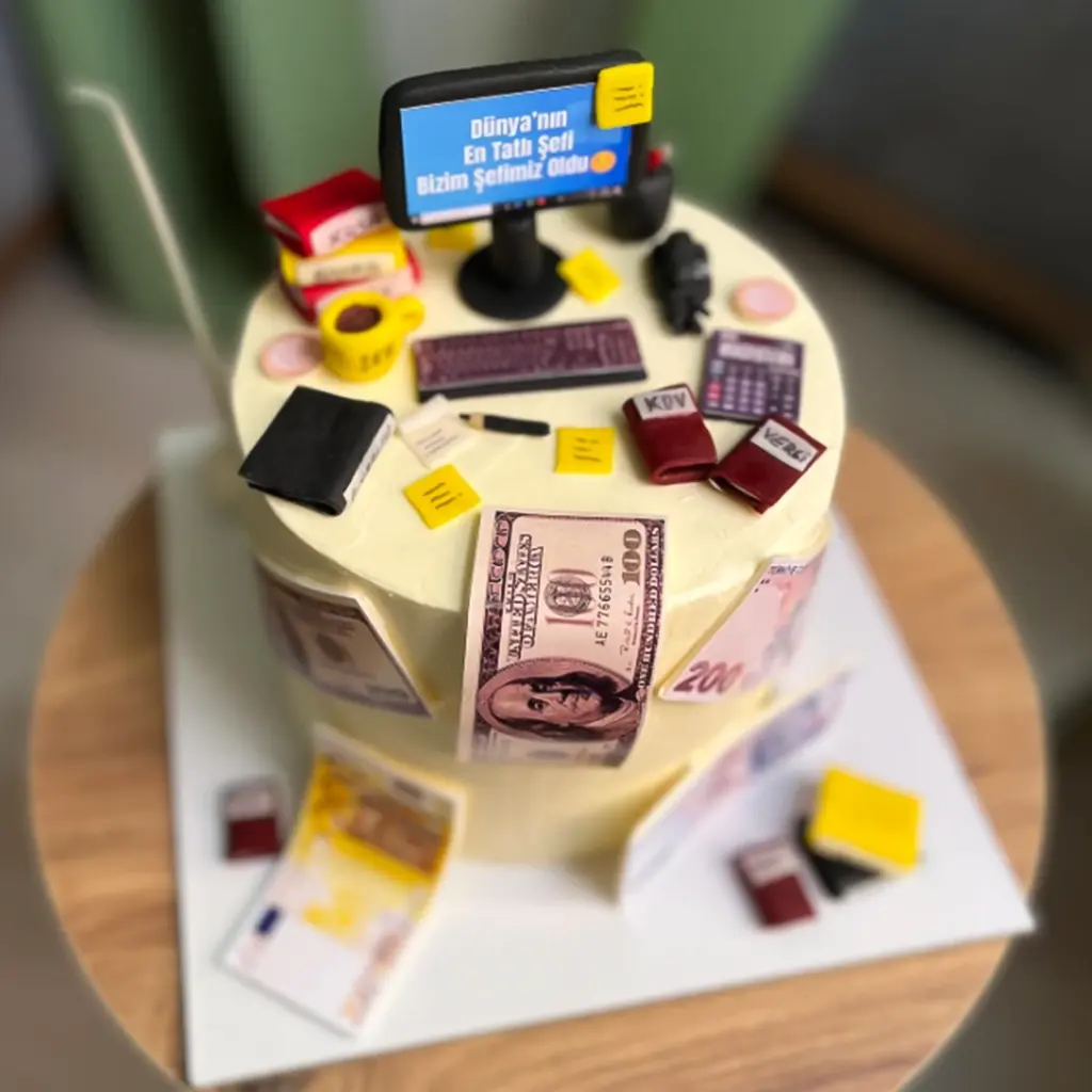 Ofis temalı, iki katlı sarı kremalı pasta üzerinde minyatür bilgisayar, klavye ve para banknotları detayları.